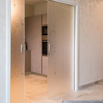 Porta scorrevole interno muro a 2 battenti in vetro temperato con rifiniture in legno laccato, maniglie adesive JNF